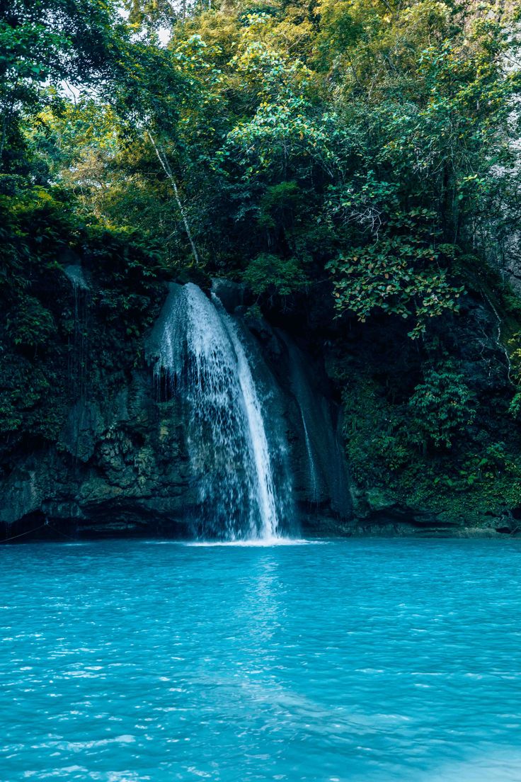 a waterfall in the middle of a body of water with trees on either side and blue water below