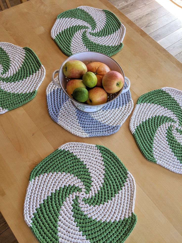 four crocheted placemats with apples and pears in a bowl on a wooden table