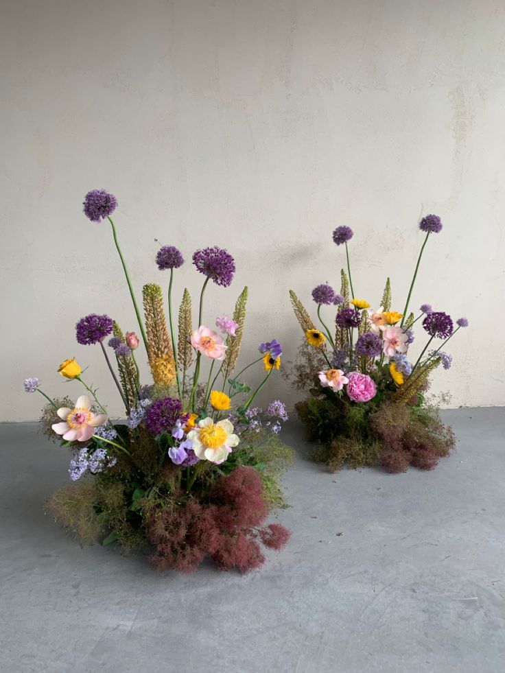 two vases filled with different colored flowers on top of a cement floor next to each other