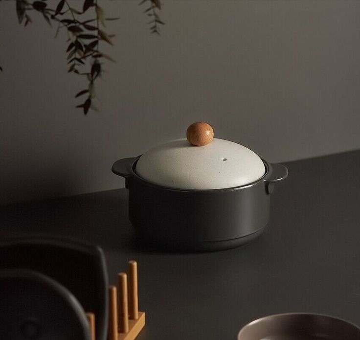 a pot with a wooden lid sitting on top of a table next to plates and bowls