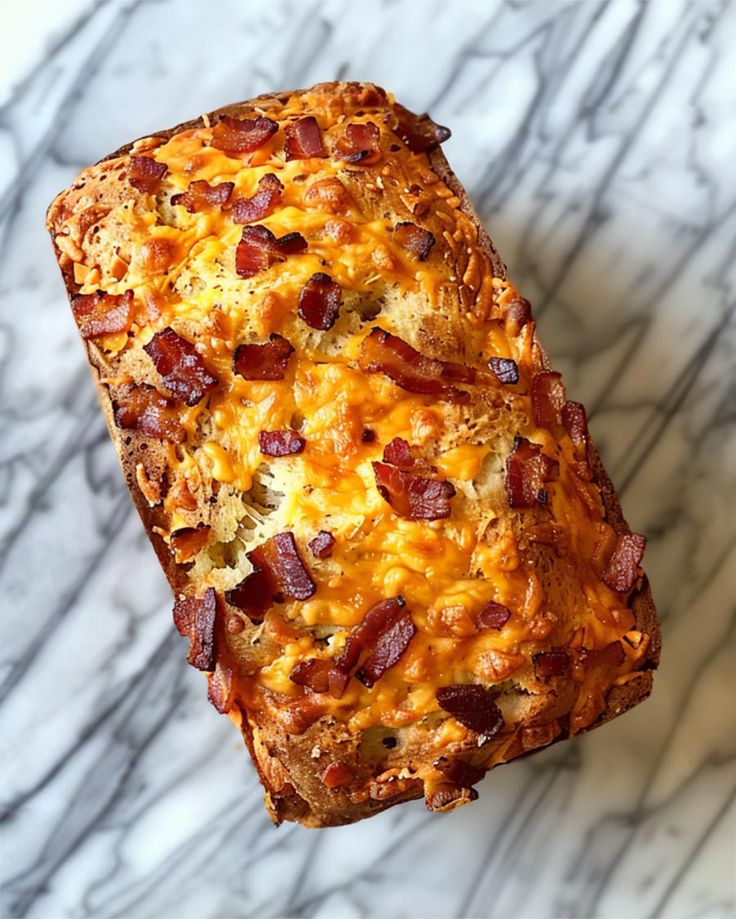 a piece of bread that is sitting on a marble counter top with cheese and bacon in it