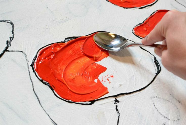 a person is using a spoon to paint an orange piece of art on a white surface