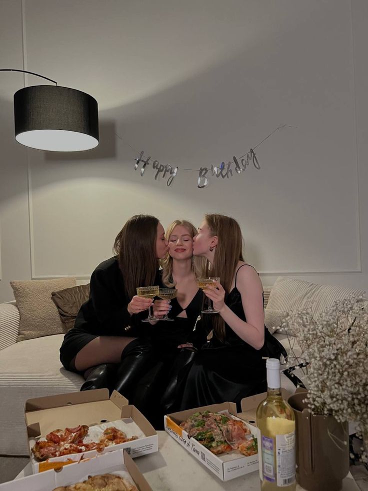 three women sitting on a couch drinking wine and eating pizza