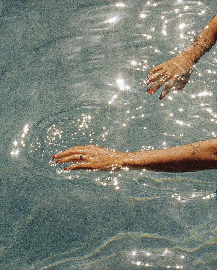 a person in the water reaching out to grab something from their hand, with sunlight shining on them