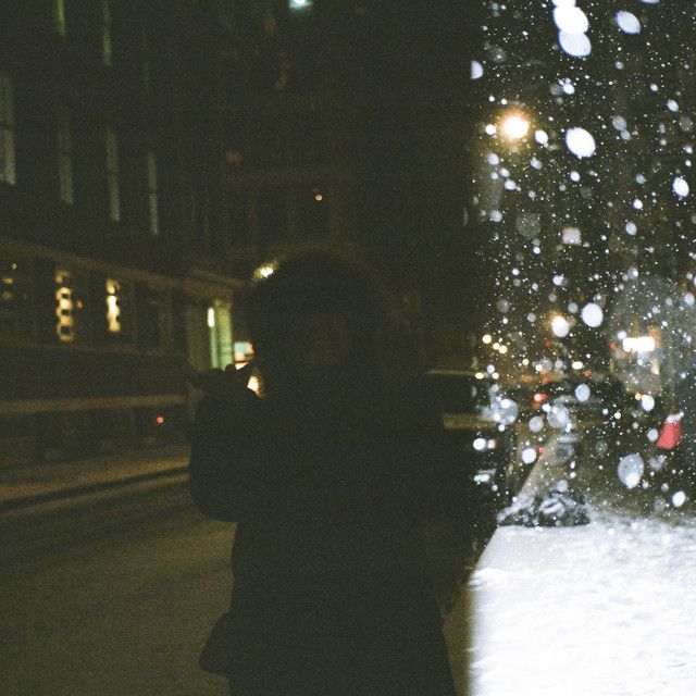 a woman standing in front of a snow covered christmas tree at night with the lights on