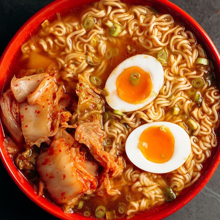 a red bowl filled with noodles, meat and two boiled egg halves on top of them