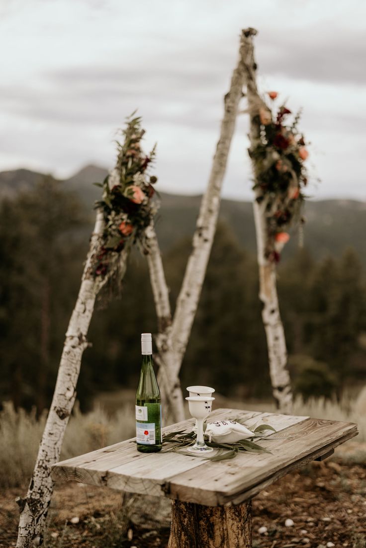 a wooden table topped with a bottle of wine next to two white birch tree trunks