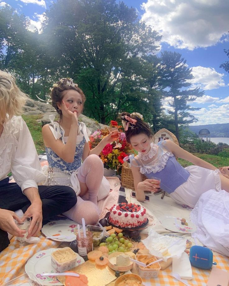 three women sitting on the ground with food and drinks in front of them at a picnic