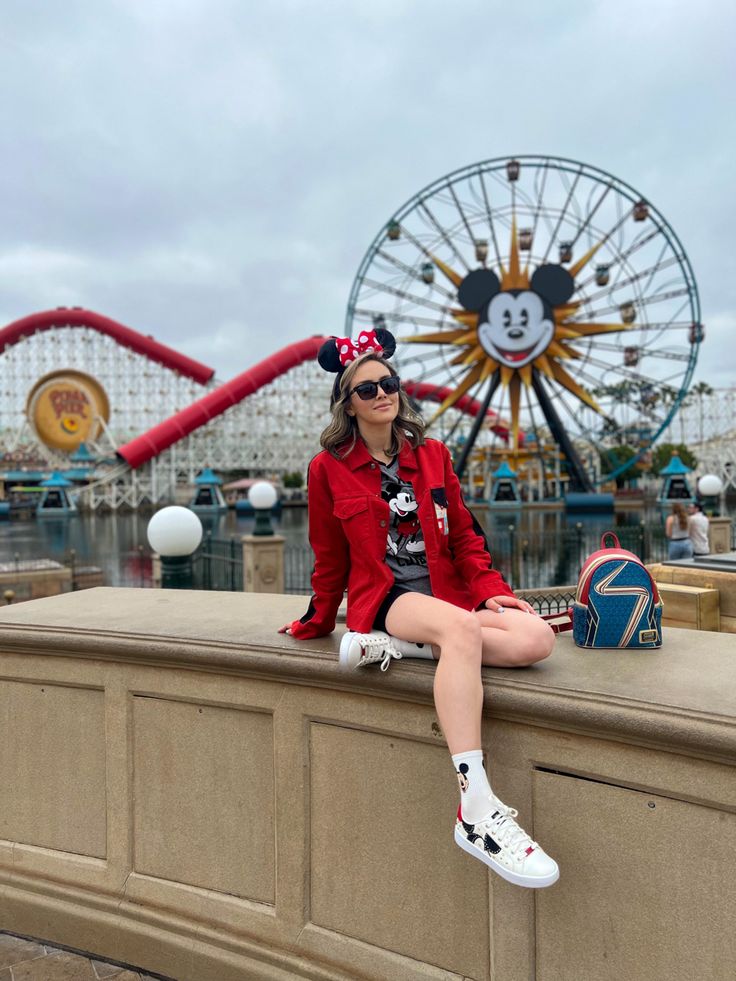 a woman sitting on top of a stone wall next to a carnival park ferris wheel