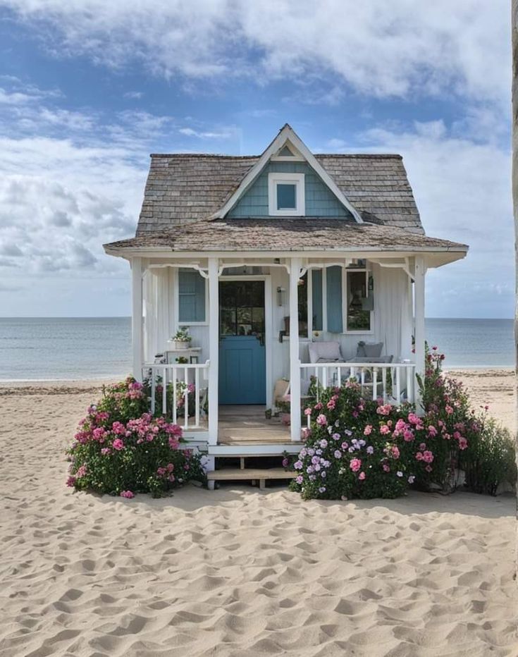 a small house on the beach with flowers in front