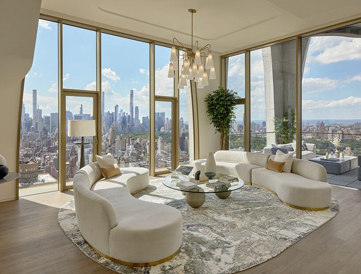 a living room filled with white furniture and tall windows overlooking the cityscape in the distance