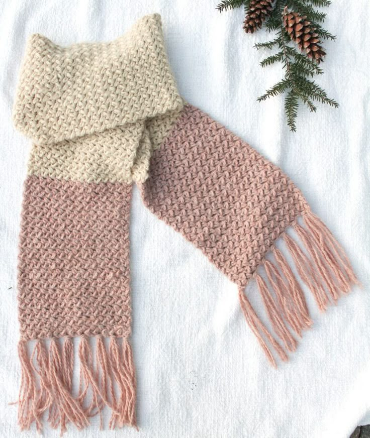 two knitted scarves sitting on top of a white towel next to pine cones