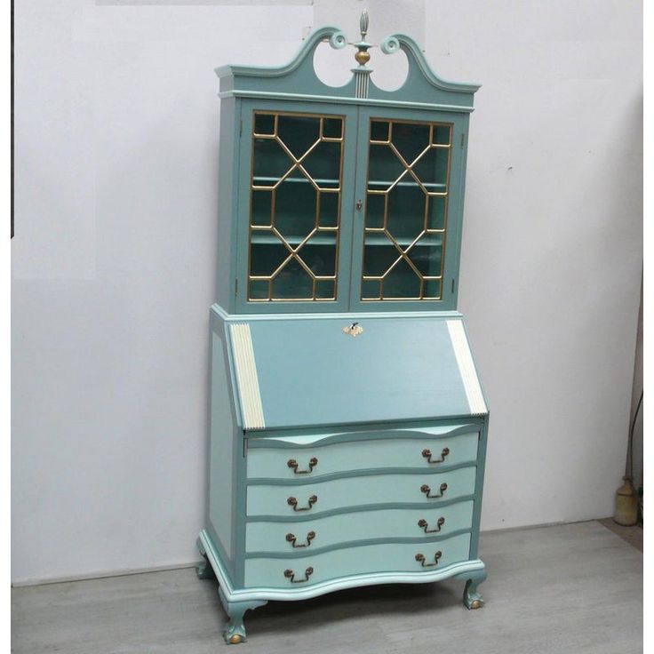 an old dresser with stained glass doors and gold trim on the top, sits in front of a white wall