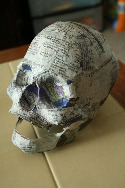 a paper mache skull sitting on top of a piece of cardboard covered in newspaper