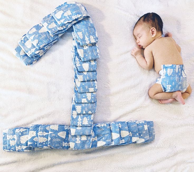 a baby laying on top of a bed next to the number one made out of diapers