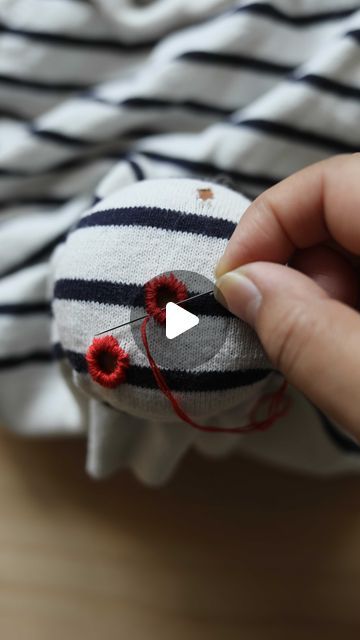 someone is stitching something on top of a striped shirt with red thread and yarn