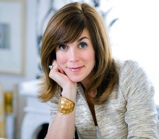 a woman sitting at a table with her hand on her chin and looking into the camera