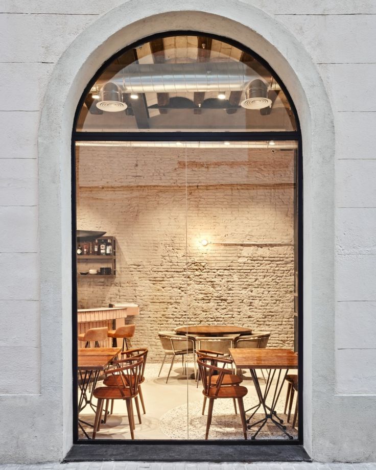 an arched window with wooden tables and chairs in front of it on a brick floor