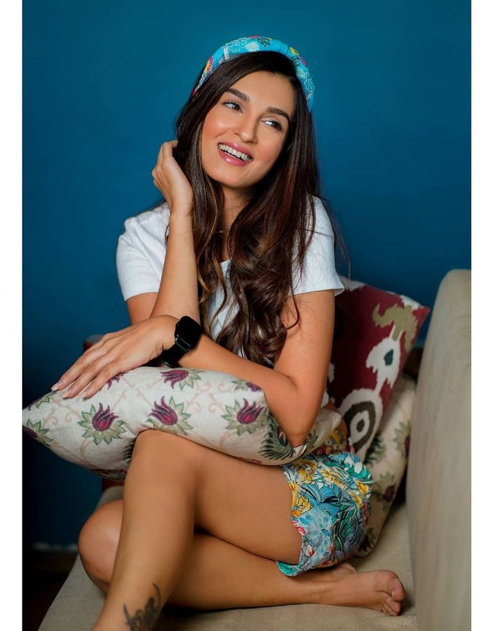 a young woman sitting on top of a couch next to a blue wall and smiling