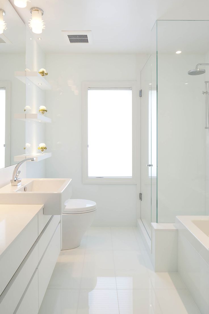 a clean white bathroom with two sinks and a toilet in the middle, along with a shower stall