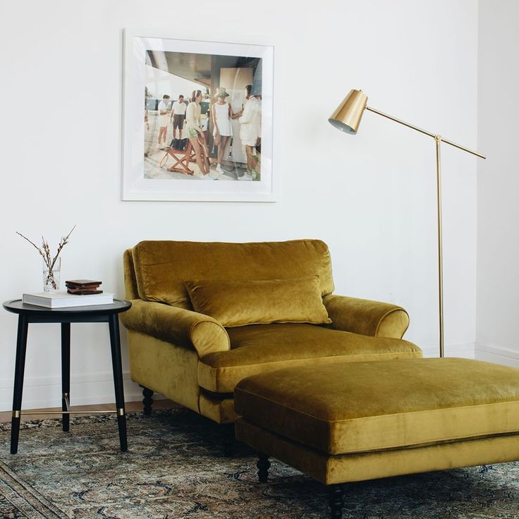 a living room with a chair and ottoman next to a lamp on a table in front of a painting