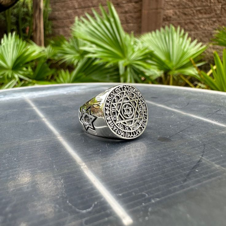 a silver ring sitting on top of a table next to some plants and trees in the background