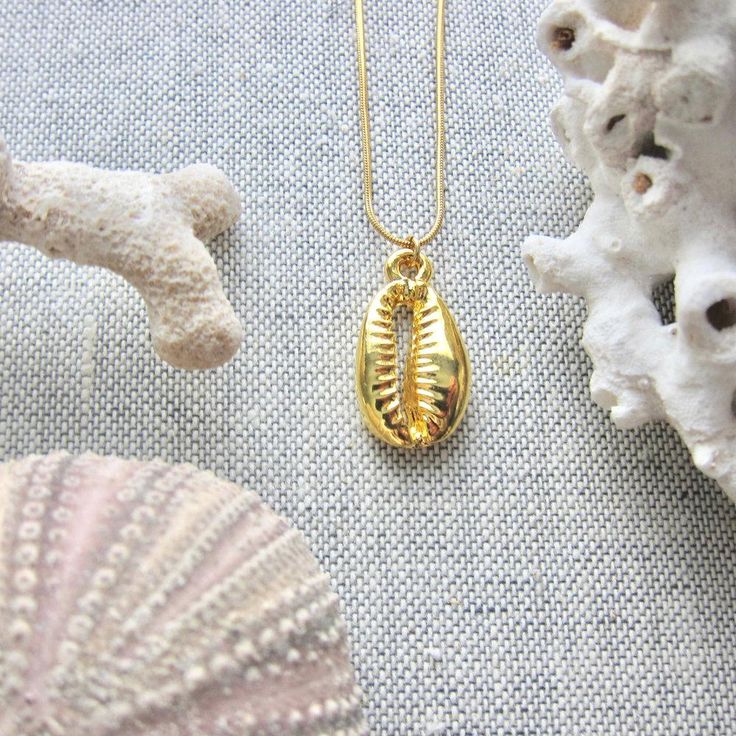 We love this fun and summery, beachy necklace. Answer the siren's song and get one for yourself or someone you love. Would make a great gift for the surfer or beach-lover in your life! A 14k gold electroplated cowrie shell dangles from a lustrous, high quality gold filled snake chain. The perfect summertime accessory! Chain: Gold fill, length 16" Cowrie Pendant: 22k Gold plated size: 26 x 18 mm✦ JEWELRY CARE ✦✧ Warm water and a soft cloth are the best thing you can do to maintain the beauty of y Dainty Shell Necklace For Beach, Ocean-inspired Yellow Gold Beach Jewelry, Beach Jewelry With Charms In Ocean-inspired Style, Dainty Shell Charm Necklace For Beach, Shell Beachy Jewelry For Summer, Ocean-inspired Jewelry With Charms For Beach, Yellow Gold Starfish Charm Jewelry For Beach, Beachy Shell Jewelry For Summer, Dainty Strand Jewelry For Beach