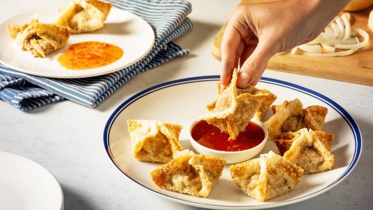 a person dipping sauce into small pieces of food on a white plate with blue trim