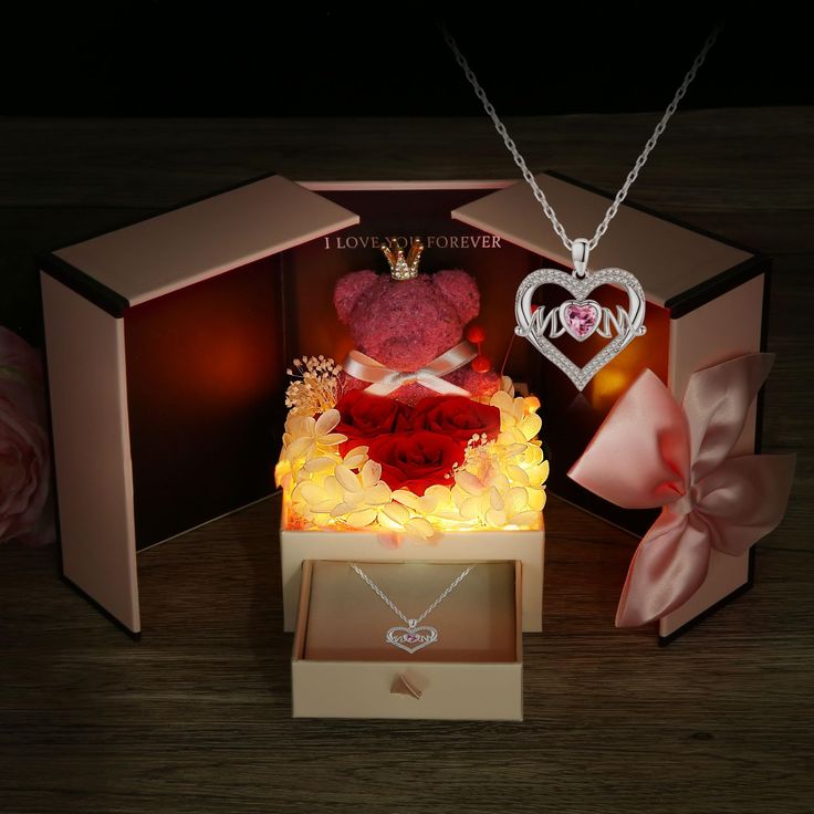 a teddy bear is sitting on top of a box with roses and a heart necklace