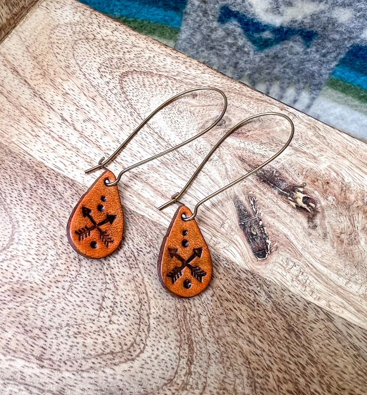 "This is a made to order listing; please allow time for its creation. Just click the Shipping & Policies tab to view our current production turnaround time! These lightweight, minimalist earrings are perfect for any outfit, every day! Stained in a rich brown and stamped with a classic crossed arrow design. Hoop earring is made of brass. *The back of your earrings are the softer, textured suede and do not accept impressions. Leather portion of earring measures about 1/2\" tall. *Measurements are Artisan Brown Teardrop Earrings, Adjustable Rust Earrings With Ear Wire, Minimalist Brown Earrings For Gift, Minimalist Brown Leather Earrings, Brown Leather Minimalist Earrings, Rustic Brown Teardrop Jewelry, Everyday Hypoallergenic Brown Jewelry, Artisan Brown Earrings For Pierced Ears, Handmade Brown Earrings For Everyday Use