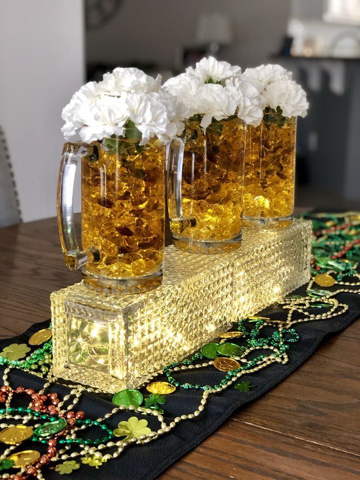 three glasses filled with beer sitting on top of a table covered in flowers and beads