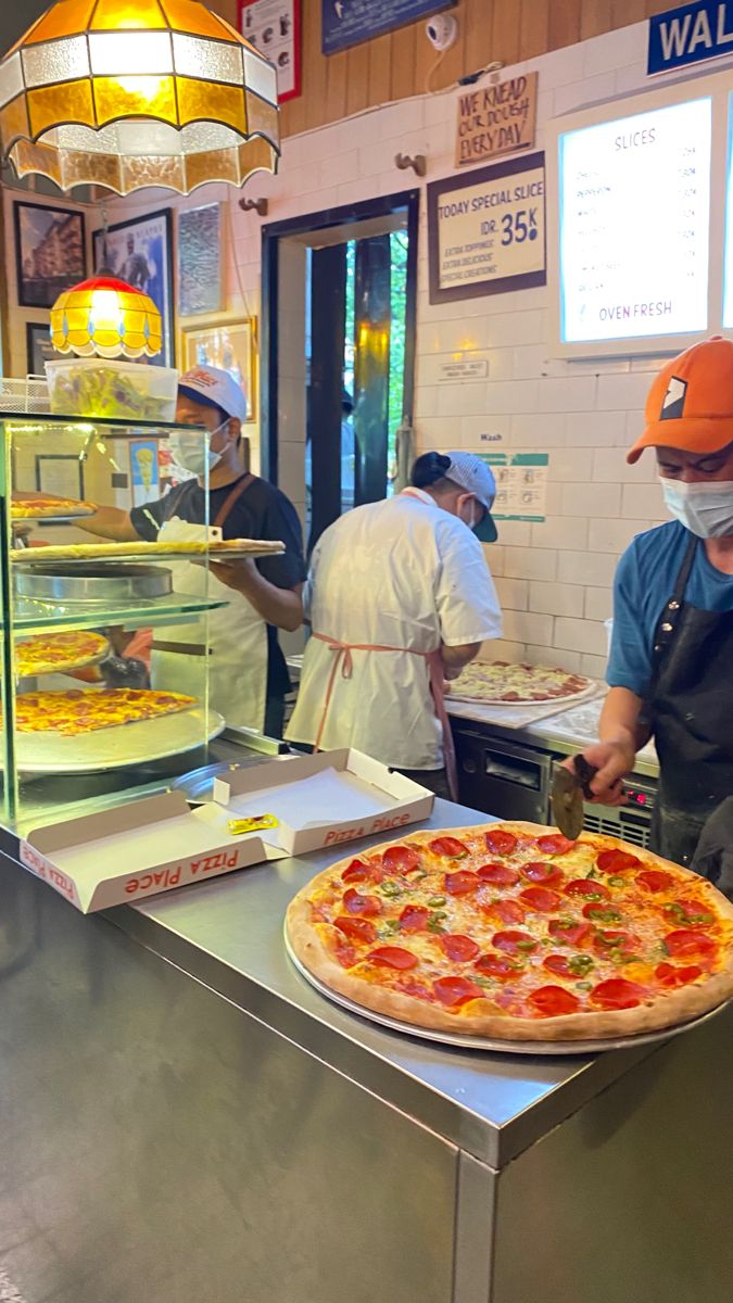 a man wearing a face mask in front of a pizza on a counter at a restaurant