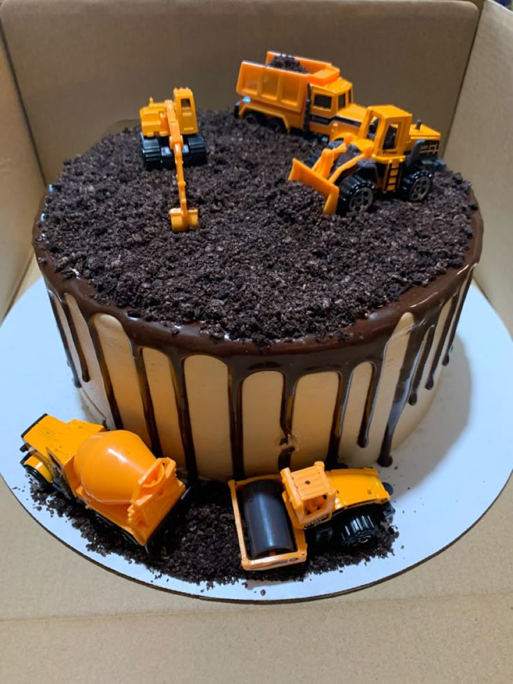 a chocolate cake with construction trucks and dirt on the top is in a cardboard box