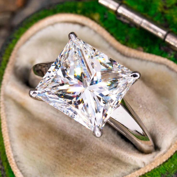 a white diamond ring sitting on top of a piece of cloth next to a pen