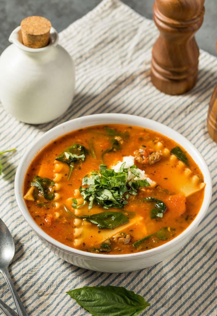 a white bowl filled with pasta and spinach soup next to a salt shaker