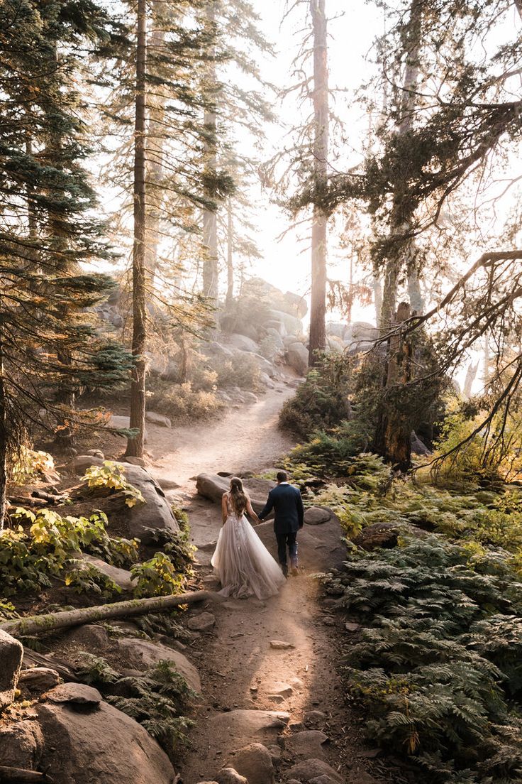 a bride and groom walking down a path in the woods