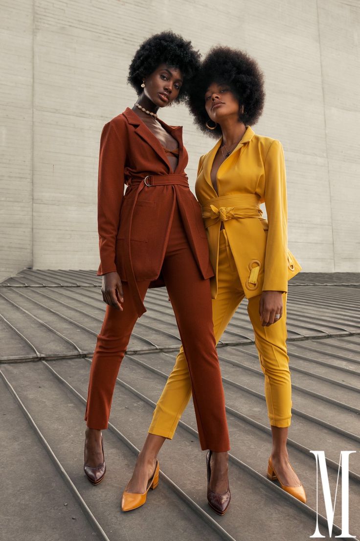 two women standing next to each other in front of a white wall wearing yellow outfits