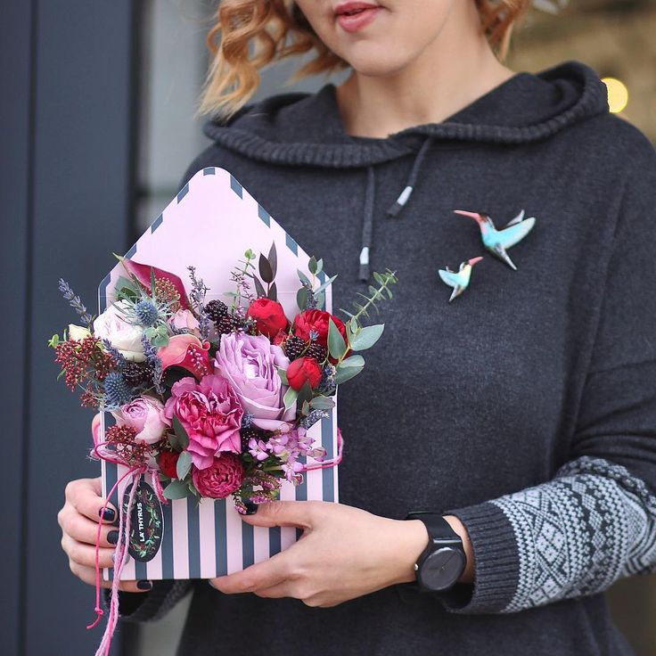 a woman holding a bouquet of flowers in front of a house shaped card box with hummings on it