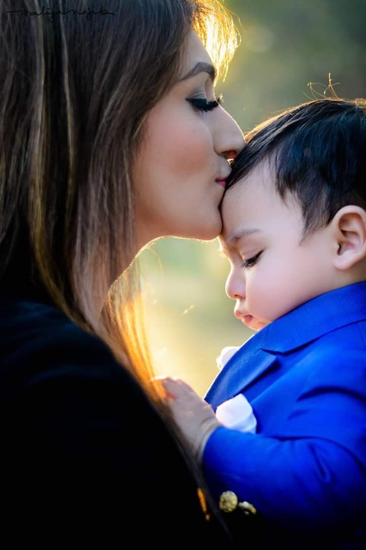 a mother kissing her son's cheek with the sun shining behind them in the background