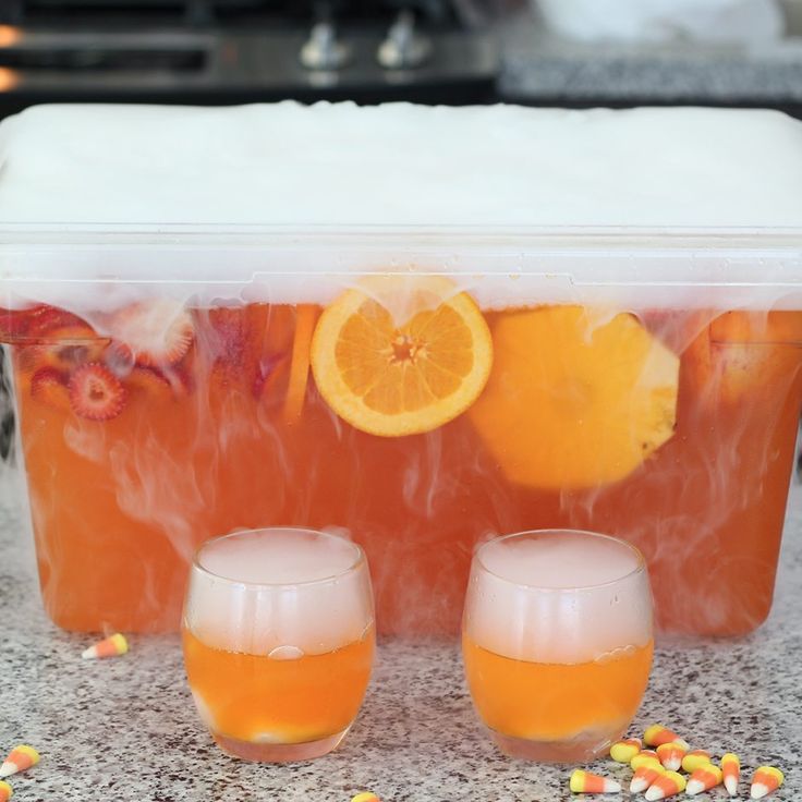 two glasses filled with liquid next to oranges and corn on the counter top in front of an ice chest