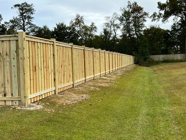 a long wooden fence in the middle of a grassy area with trees and bushes behind it