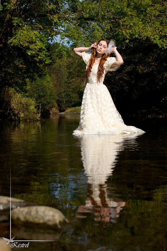 a woman in a white dress is standing in the water with her hands behind her head