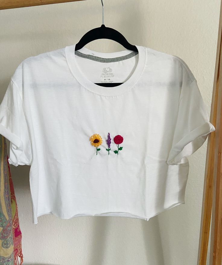 Thank you for your interest! This item is a hand embroidered cropped tee. The sleeves are tiled and stitched and the bottom is a raw edge. The design is 3 different flowers a sun flower, a rose and a lavender branch.  -Men's T-shirt  -size men's M  -Fruit of the loom  -hand embroidred  colors: green, brown, yellow, red, purple White Tee Embroidery, Casual Floral Embroidery Crop Top For Spring, Spring Cotton Crop Top With Floral Embroidery, Spring Floral Embroidery Cotton Crop Top, Casual Cotton Crop Top With Floral Embroidery, Casual Embroidered Crop Top For Summer, Trendy Tops With Custom Embroidery For Spring, Trendy Top With Custom Embroidery For Spring, Casual White Embroidered Crop Top