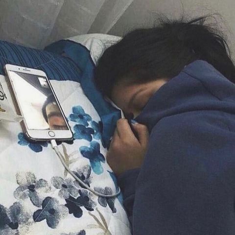 a woman laying in bed with her head on the pillow next to an electronic device