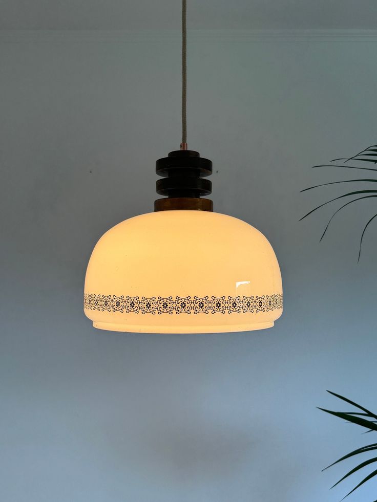 a white light hanging from a ceiling in a room with potted plants on the side