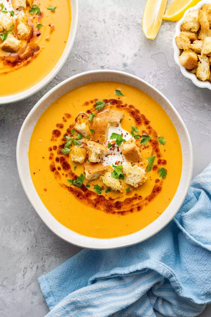 two bowls of soup with bread and garnishes on the side, next to a bowl of croutons