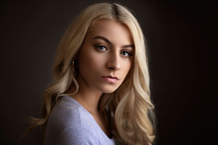 a woman with blonde hair and blue eyes posing for a photo in front of a dark background