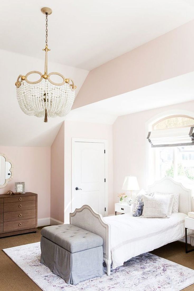 a bedroom with pink walls, white furniture and a chandelier hanging from the ceiling