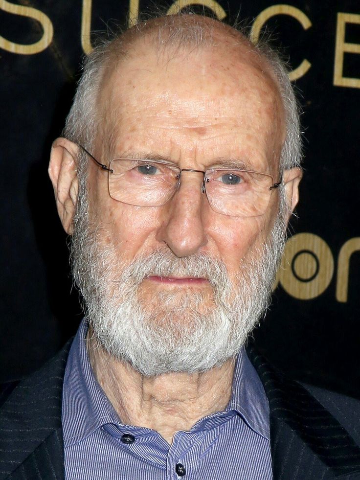 an older man with glasses and a beard is looking at the camera while standing in front of a black backdrop