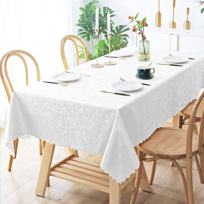 a dining room table with white linens and place settings on the table, in front of a potted plant